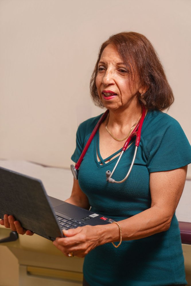 Dr. Maria Soto in scrubs at Ivy League Pediatrics, laptop in hand